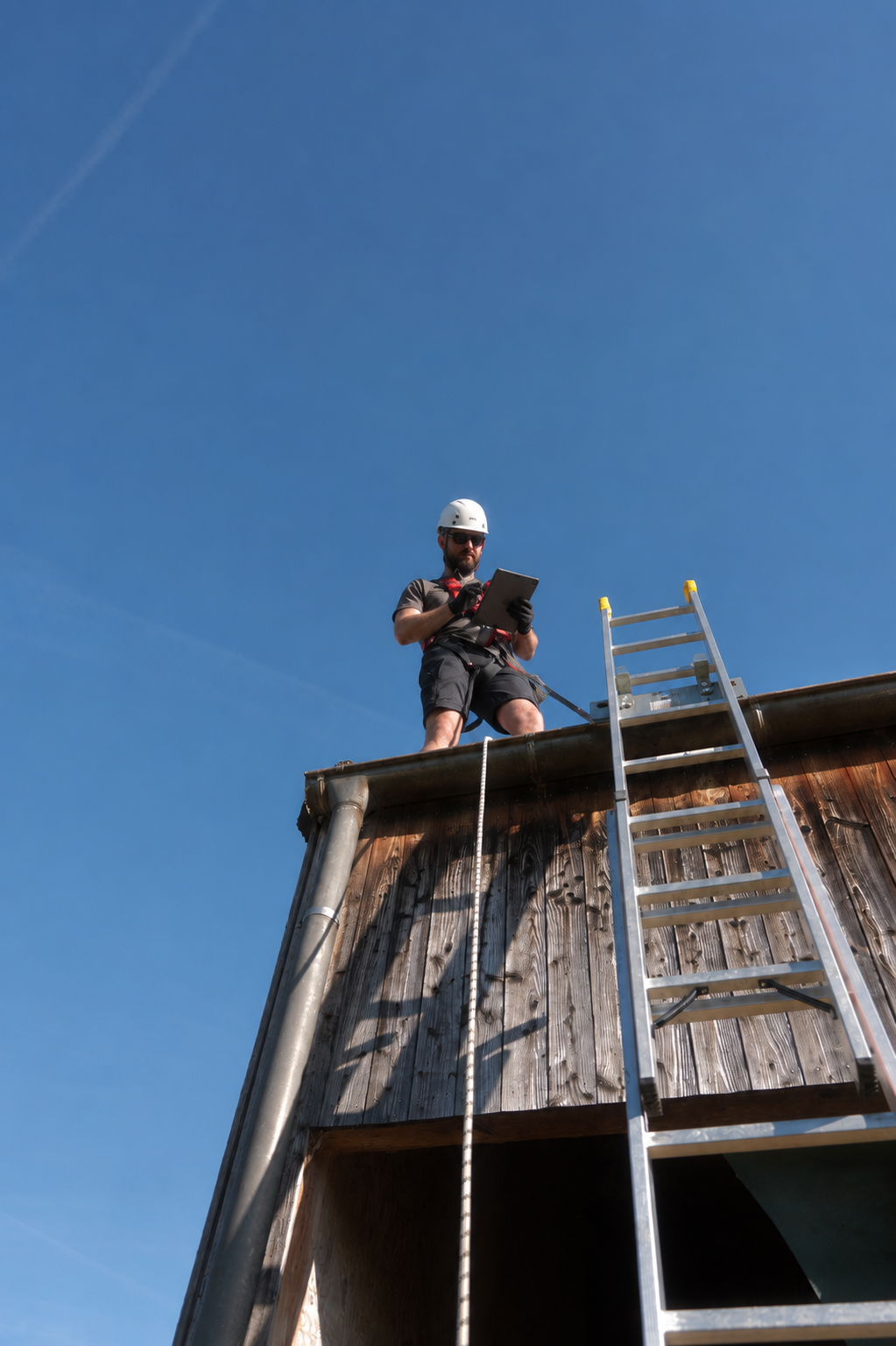 Techniker mit Helm und Auffanggurt auf einem Dach gesichert über Leiter